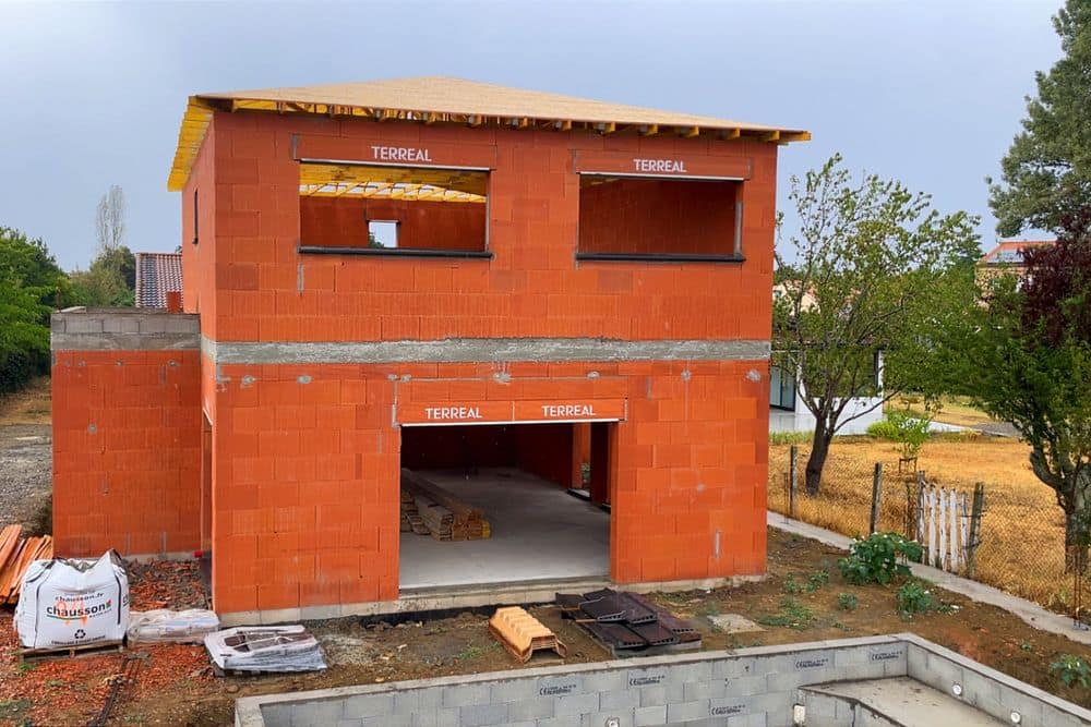 Maison en brique achevée en élévation, charpente posée et linteaux apparents