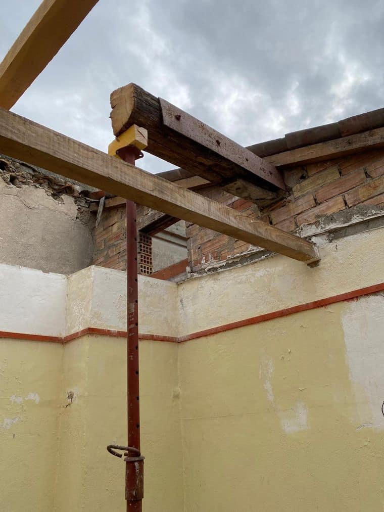 Étai métallique sous une poutre ancienne, murs en brique et enduit d’une maison ancienne en rénovation