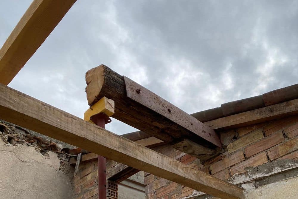 Étai métallique sous une poutre ancienne, murs en brique et enduit d’une maison ancienne en rénovation