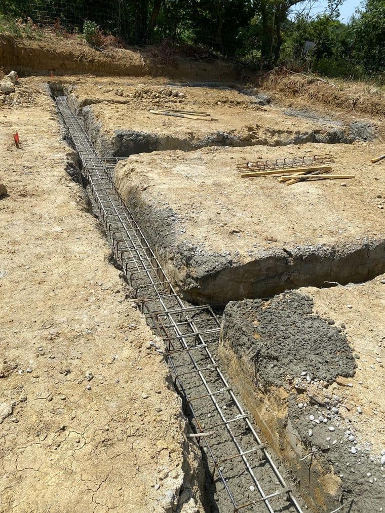 Semelles filantes coulées et amorce d’armature en attente sur un terrain en pente